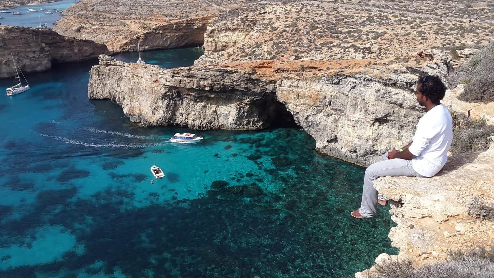 Ramesh sitting on a cliff edge above the turquoise Blue Lagoon