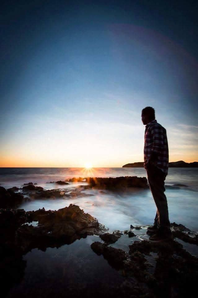 Silhouette of Ramesh on a rocky shore at sunset